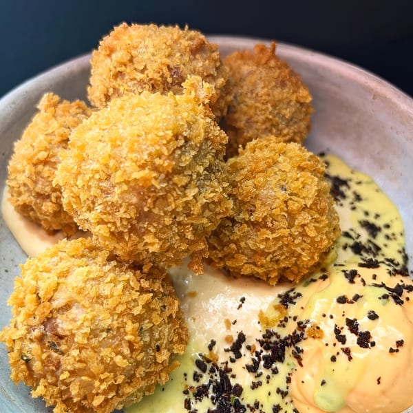 Six golden-brown Peruvian croquettes with a crispy coating, served with two creamy sauces and dark sprinkles.