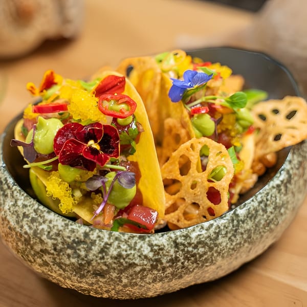 Colorful Peruvian tacos with edible flowers, avocado, and fish roe in a stone bowl.