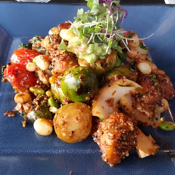 Peruvian quinoa salad with roasted vegetables, cherry tomatoes, and avocado on a blue plate.