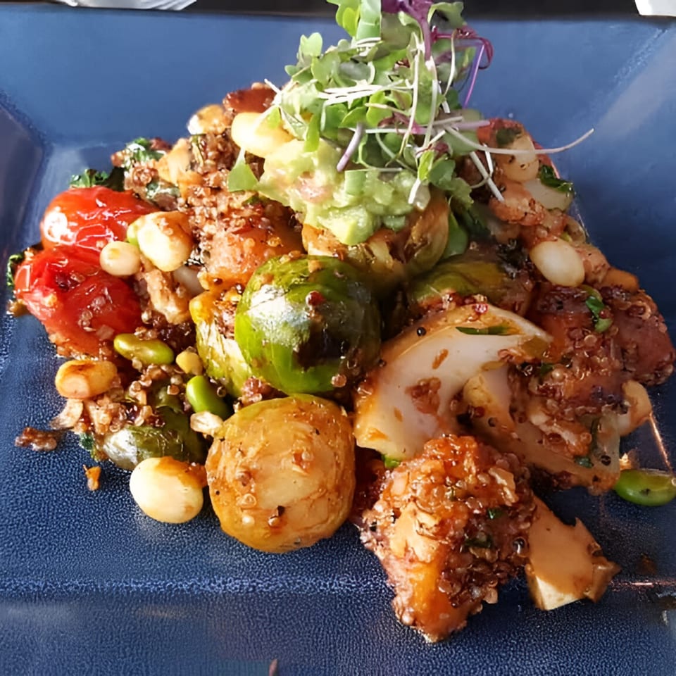 Peruvian quinoa salad with roasted vegetables, cherry tomatoes, and avocado on a blue plate.
