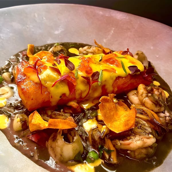 Peruvian seafood dish with salmon, shrimp, mussels, and sweet potato chips in a dark sauce.