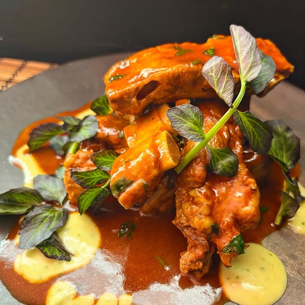 Peruvian-style chicken in a rich orange sauce with green herbs and yellow cream on a dark plate.