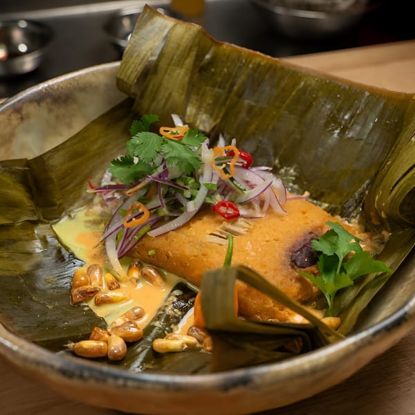 Peruvian tamale, garnished with red onion, cilantro, and chili, served in a banana leaf.