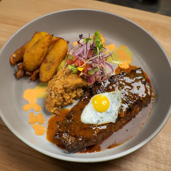 Peruvian lomo saltado with a fried egg, rice, plantains, and a fresh salsa on a gray plate.