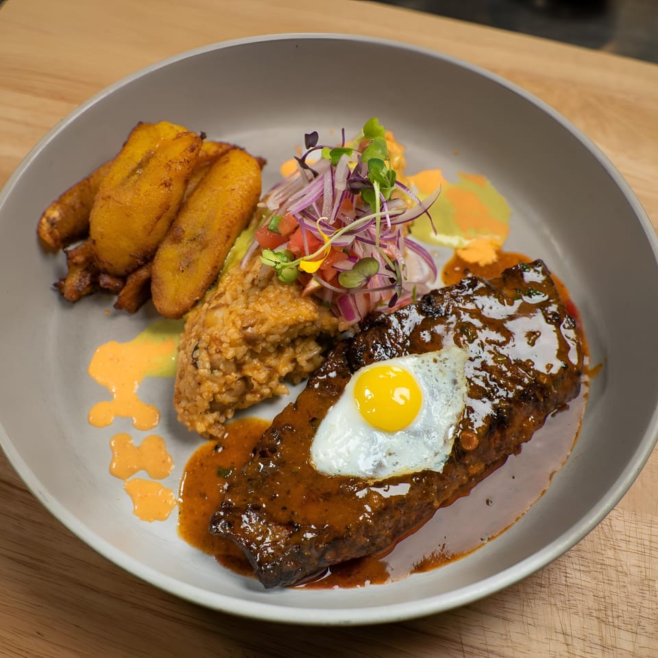 Peruvian lomo saltado with a fried egg, rice, plantains, and a fresh salsa on a gray plate.