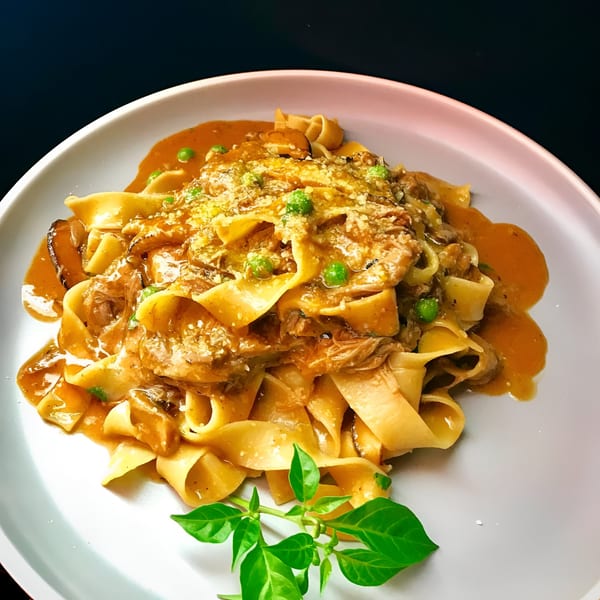 Peruvian pappardelle pasta with a rich sauce, peas, and fresh basil on a white plate.