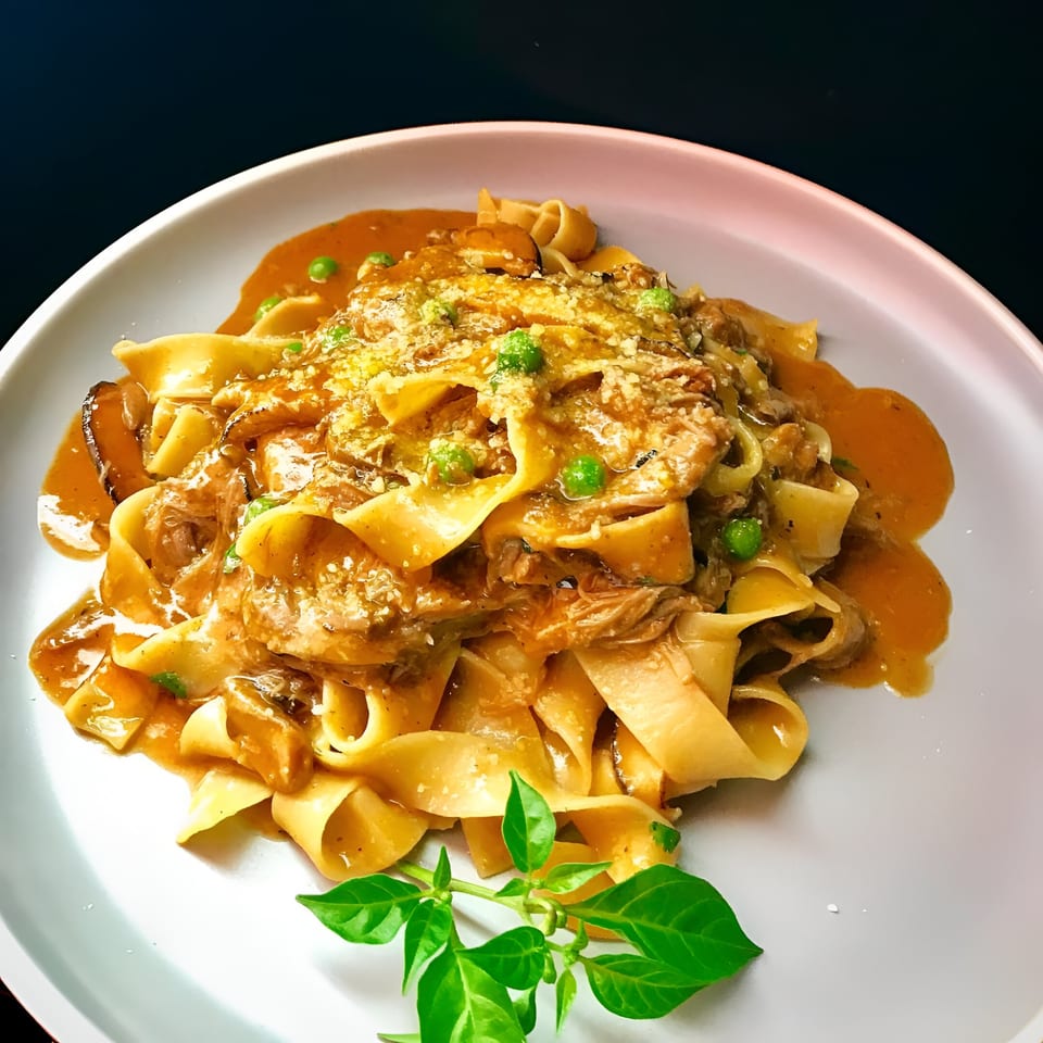 Peruvian pappardelle pasta with a rich sauce, peas, and fresh basil on a white plate.